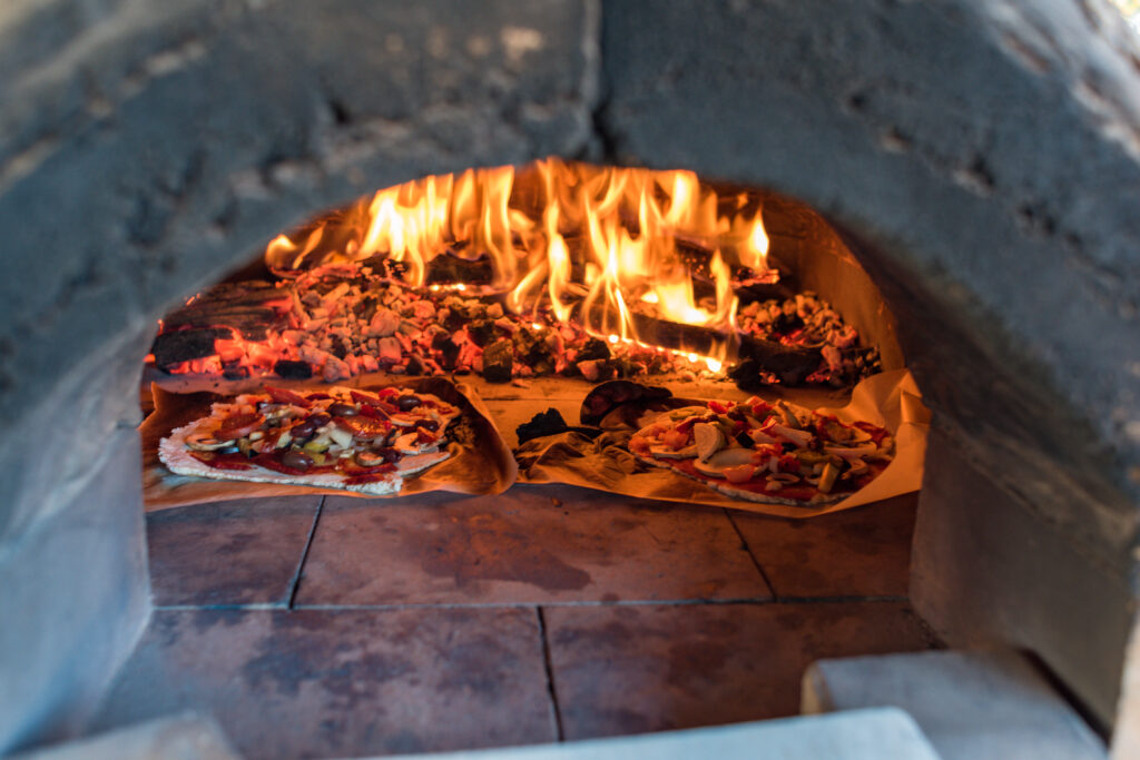 Italian pizza cooking in pizza oven over open flame