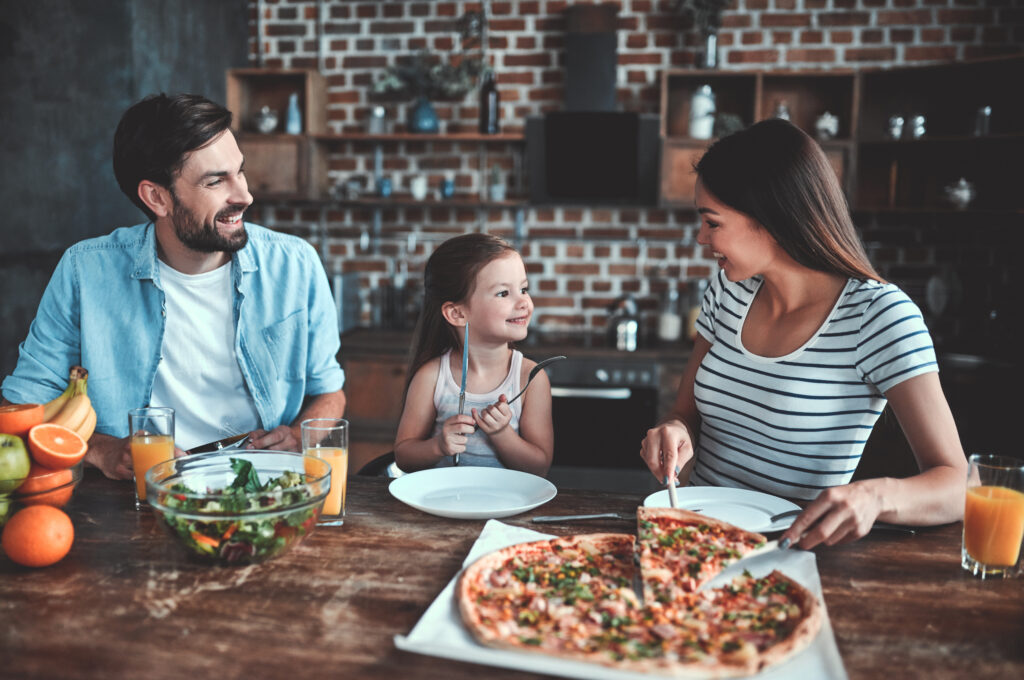 Mom, dad and daughter are eating pizza together on kitchen