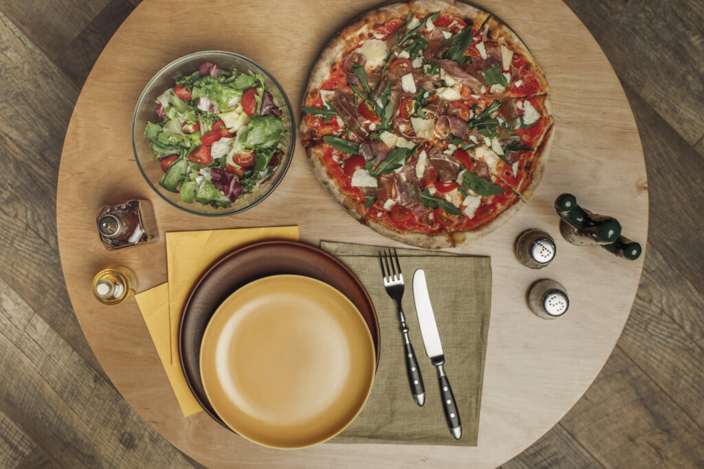 top view of arrangement of empty plates, pizza and salad on wooden table