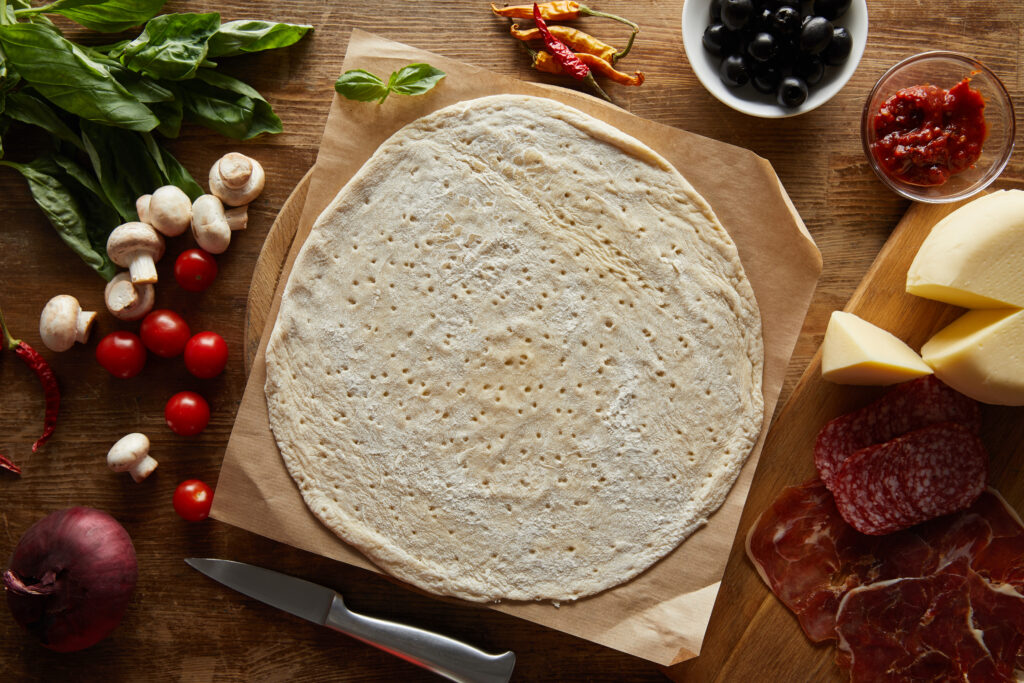 top view of raw dough with ingredients for pizza on wooden table