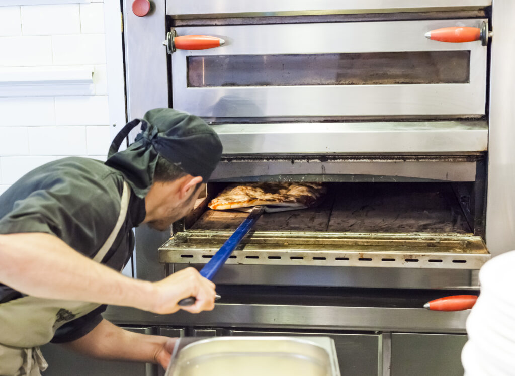 Chef baker in black uniform baking a pizza in the oven at a restaurant kitchen.