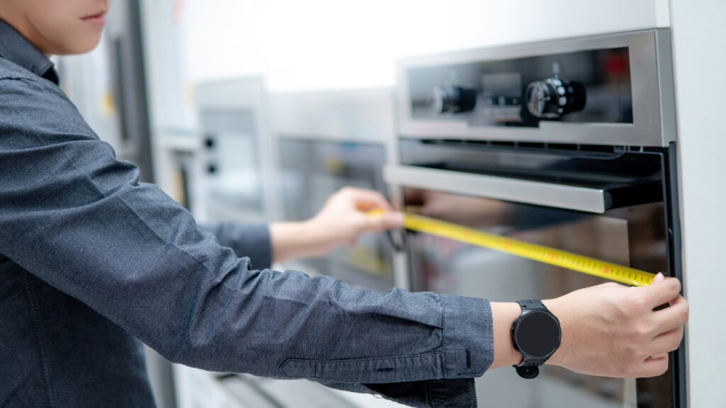  man using tape measure on oven in the kitchen showroom in furniture store