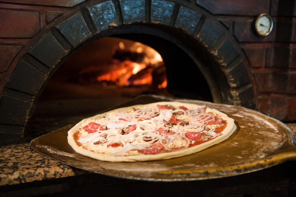Close up view of cooking process of raw pizza on wooden stove in brick oven
