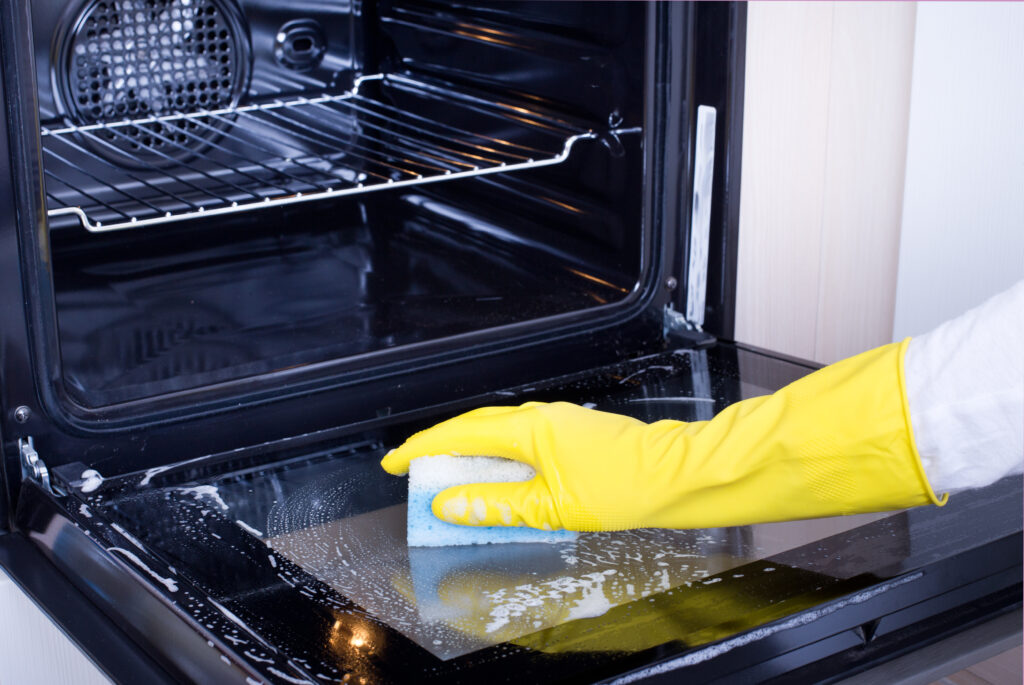 Close up of female hand with yellow protective gloves cleaning oven 