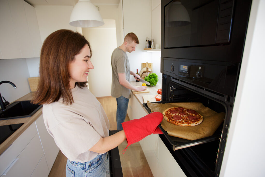 woman monitoring pizza in the oven